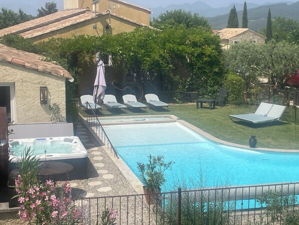 A swimming pool with lounge chairs, a hot tub, and a stone pathway.