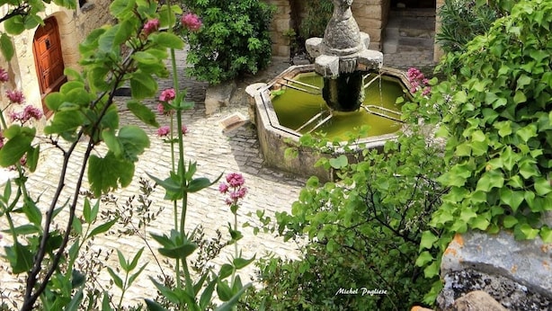 Un bâtiment en pierre doté d’une cour, d’une fontaine et d’une statue.