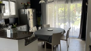 Une cuisine moderne avec un coin repas, comprenant un îlot central, des meubles blancs et une grande fenêtre agrémentée de rideaux légers.