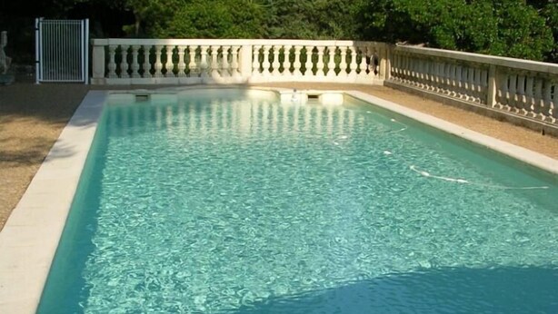 Ein rechteckiger Swimmingpool mit klarem, blauem Wasser, umgeben von einer weißen Fliesenveranda und einem dekorativen Steinbalustraden.
