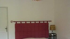 Ein Schlafzimmer mit einem roten Kopfteil, einem Bett mit einer rosa Decke, einer Lampe auf einem Nachttisch und einer Tür.