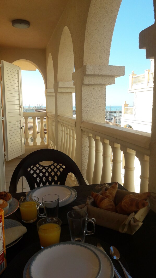A balcony with a table set for breakfast, including croissants, orange juice, and coffee.