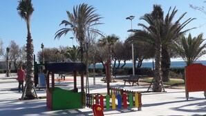 A playground with colorful play equipment, palm trees, and a bench. - Luxery apartment "SEAGULL" - Family friendly - 2 bedrooms (max.4 pers.) (El Ejido)