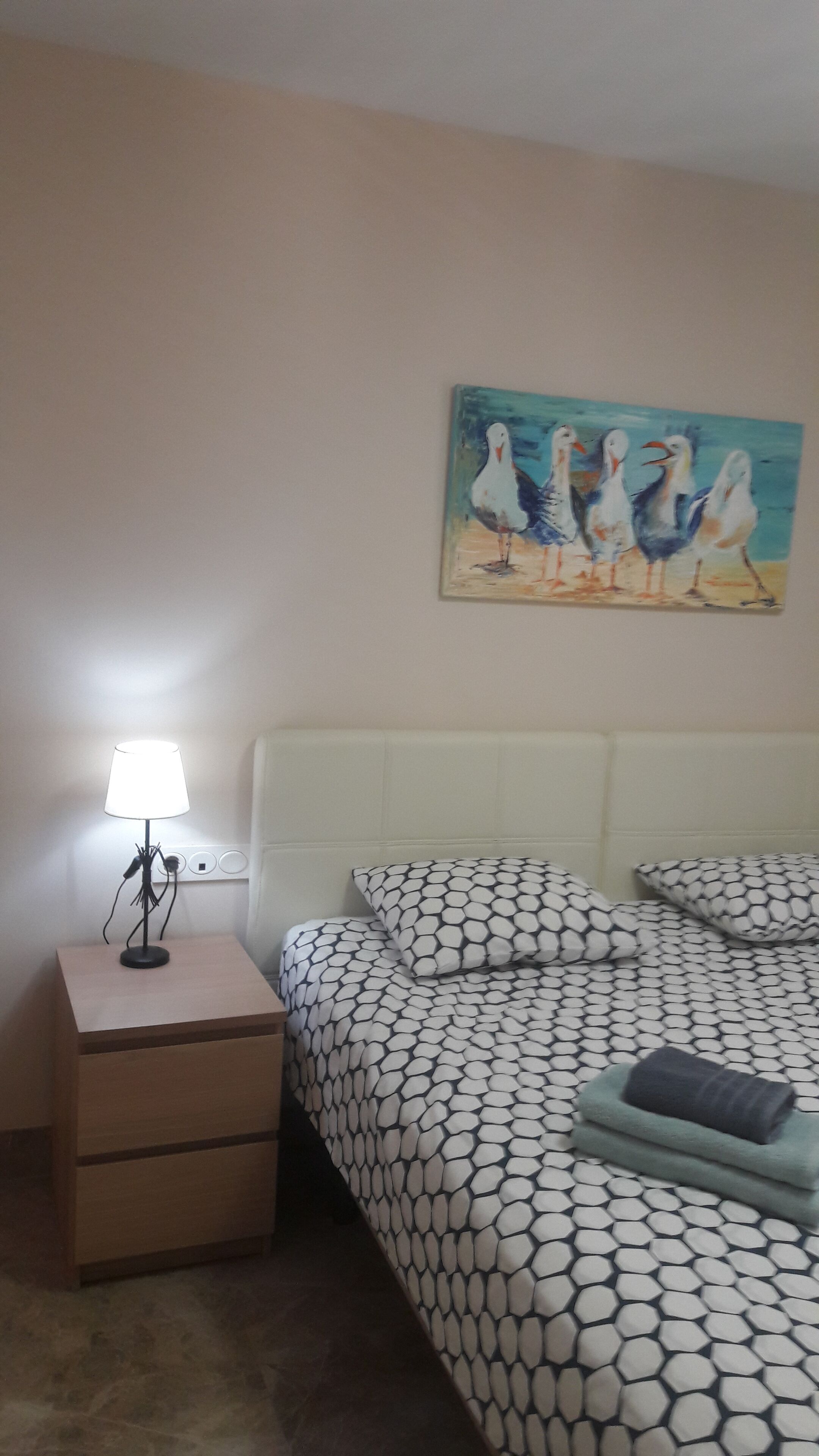 Un dormitorio con una cama, una mesita de noche, una lámpara y un cuadro en la pared.