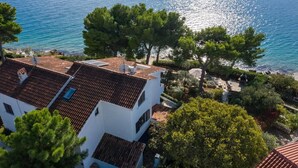 A white building with a tiled roof, surrounded by trees and a view of the sea.