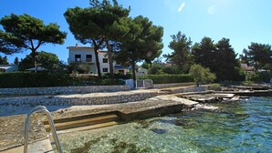 A coastal property with clear water, stone steps leading to a dock, and a white building with balconies.