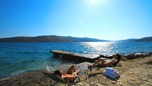 A beach with two lounge chairs and a small dock extending into the water.