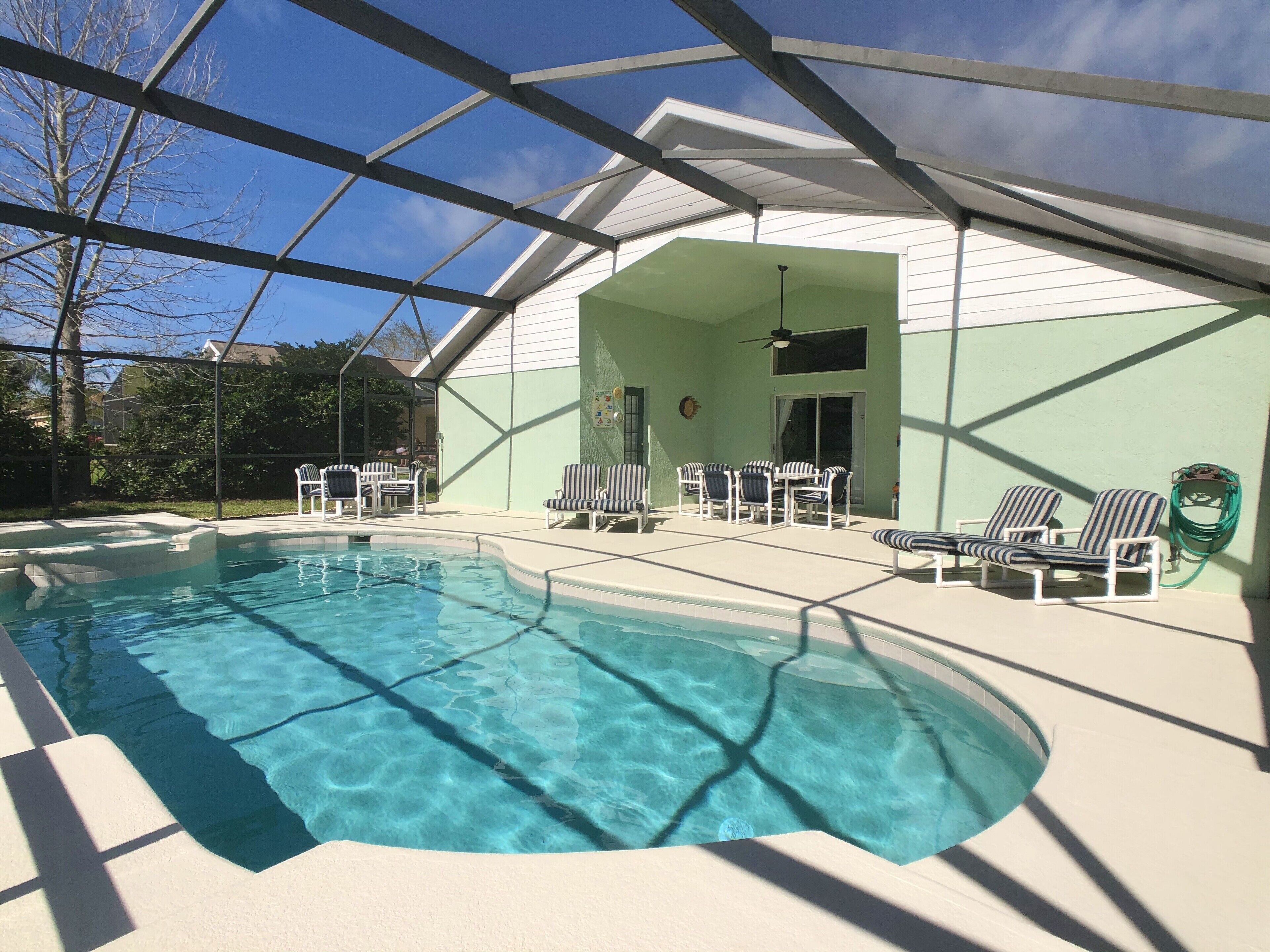 A swimming pool with clear water, surrounded by lounge chairs and a covered patio area.