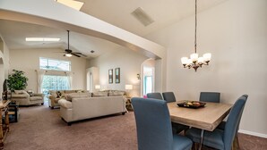 Uma sala de estar espaçosa com um sofá grande, uma mesa de jantar com cadeiras e um ventilador de teto.