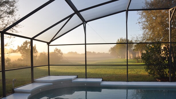 Piscina com estrutura de vidro, degraus para entrar na água e vista para uma paisagem gramada.