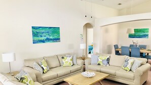 Uma sala de estar moderna com um conjunto de sofá bege, uma mesa de centro de madeira e uma área de jantar com cadeiras azuis e uma mesa de madeira.
