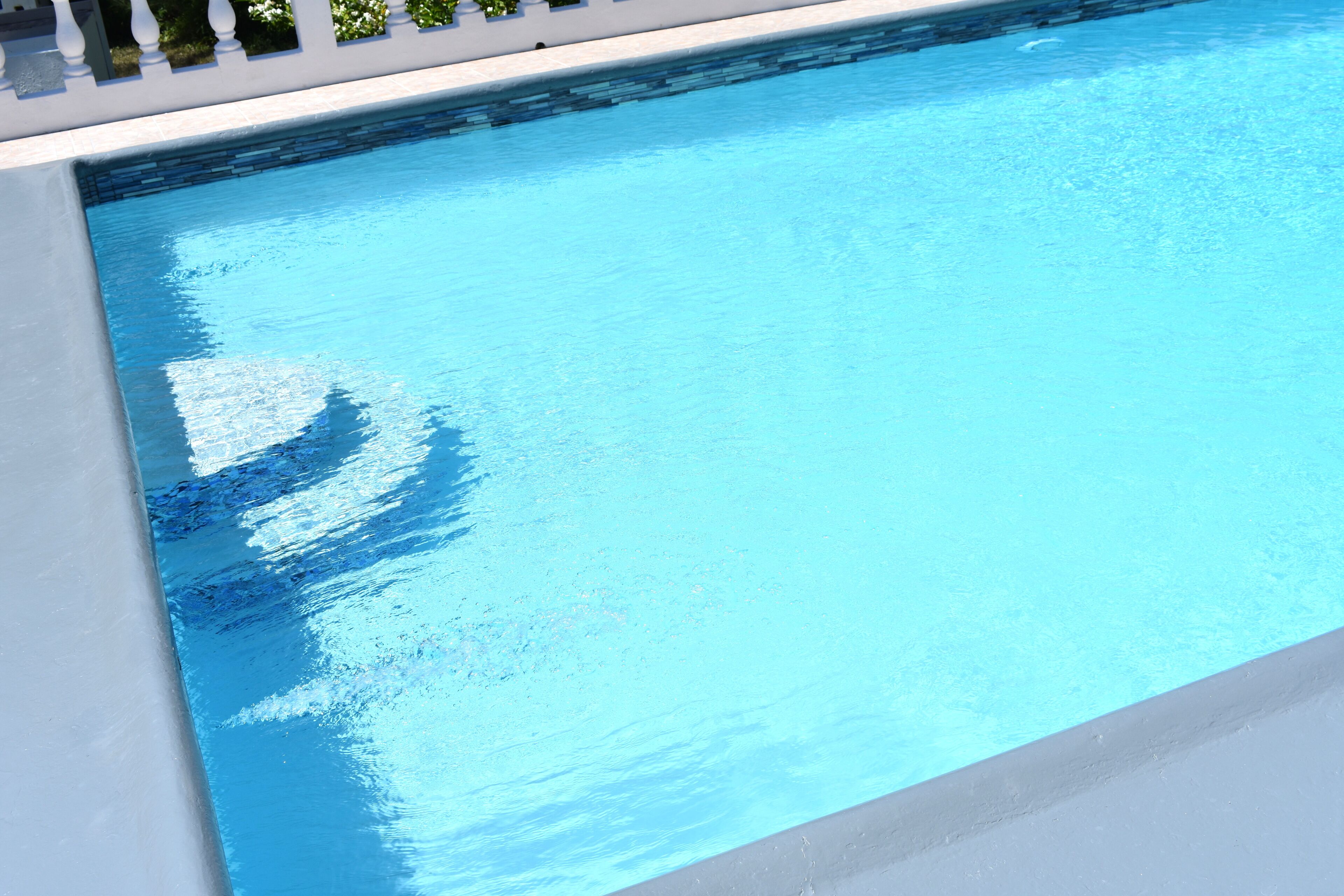 A clear blue swimming pool with a white edge and a tiled bottom.