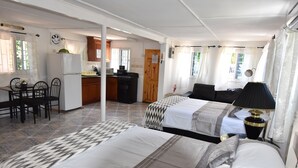 Quarto de hotel com duas camas, uma mesa de jantar com cadeiras, cozinha e vista para o exterior.