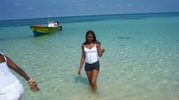 A woman walking in shallow clear water with a boat in the background.