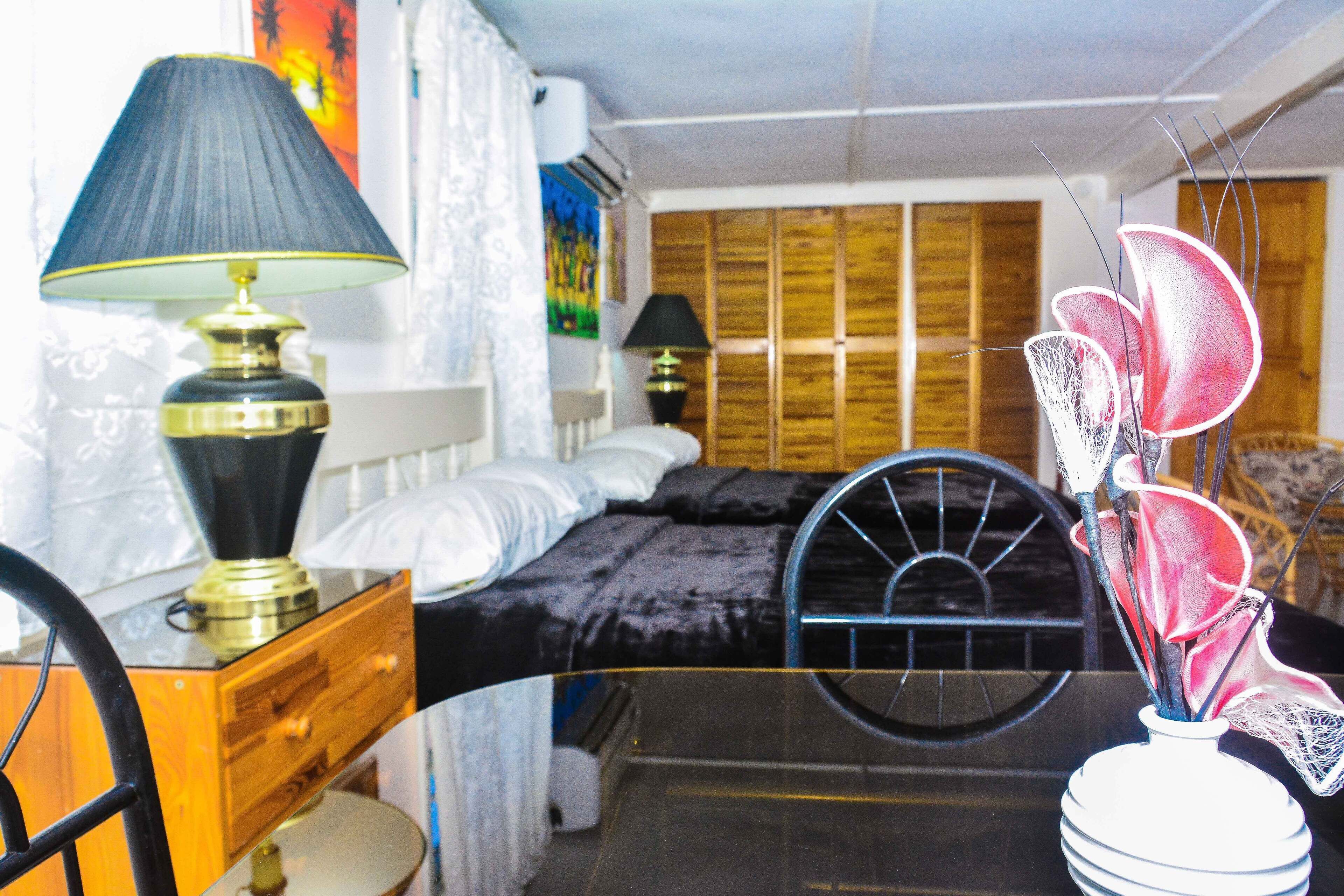 A bedroom with a bed, a desk with a lamp, a chair, and a decorative vase.