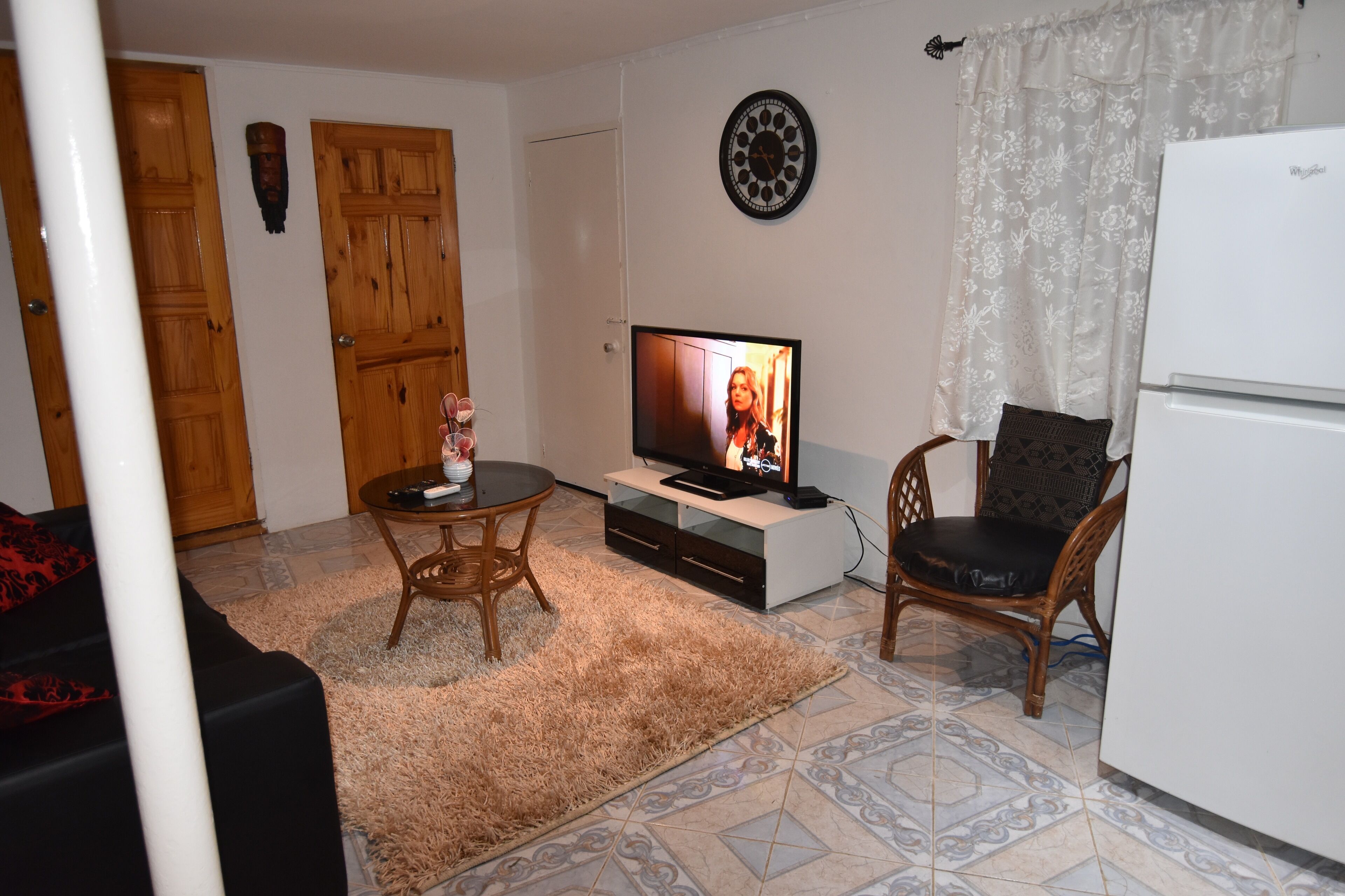 A living room with a television, a dining table, a sofa, a refrigerator, and a patterned floor.