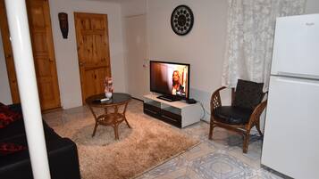 A living room with a television, a dining table, a sofa, a refrigerator, and a patterned floor.