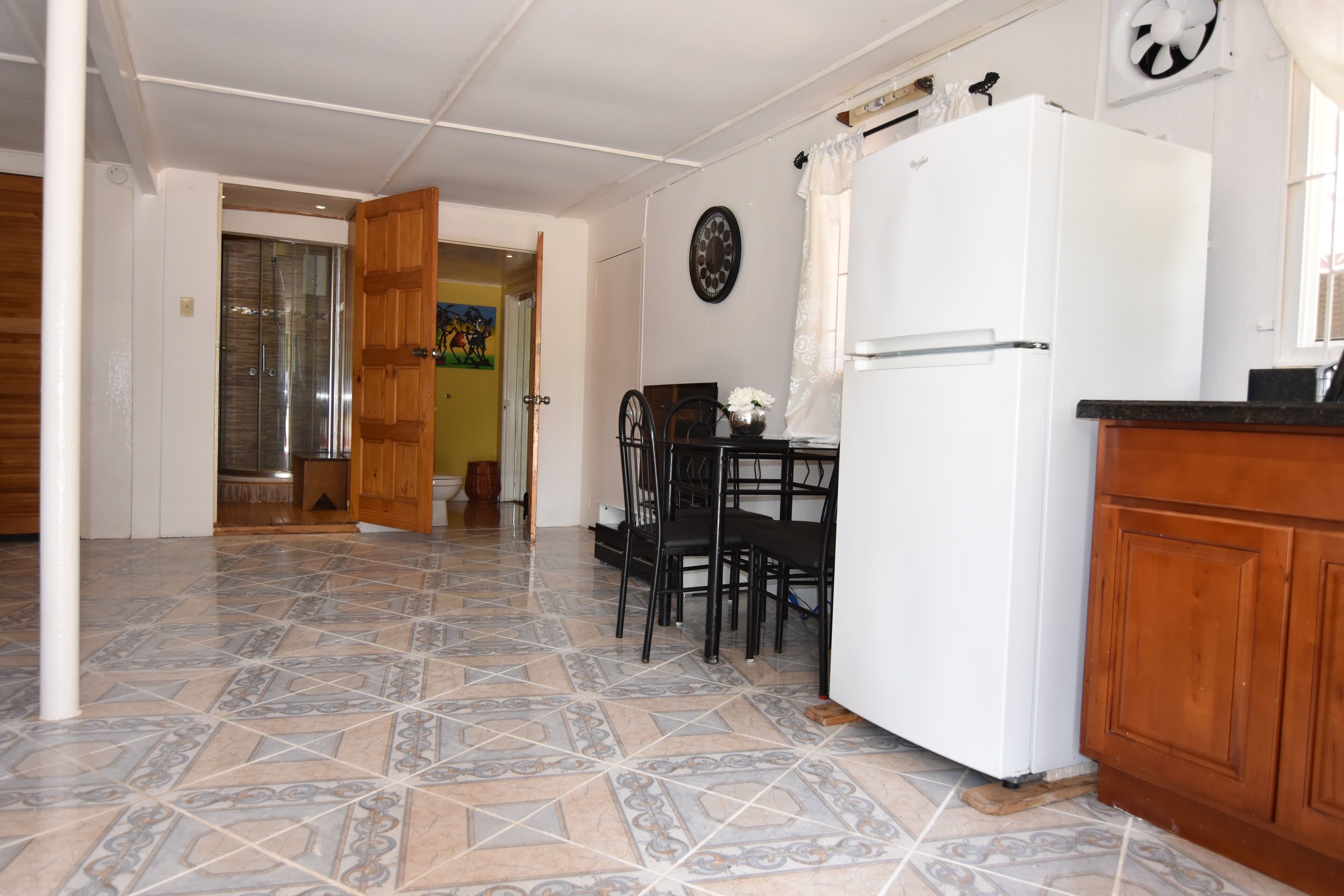 Une cuisine avec un sol carrelé, un réfrigérateur blanc, des placards en bois et un coin repas avec des chaises et une table.