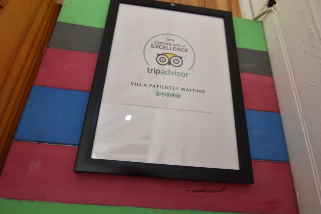 A framed certificate of excellence for TripAdvisor, Villa Patiently Waiting, with a colorful striped background.