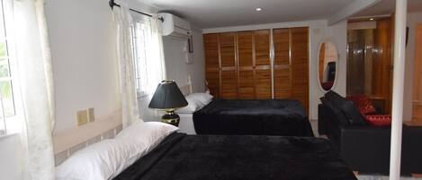 A bedroom with two beds, a wooden wardrobe, a mirror, and a window with curtains.
