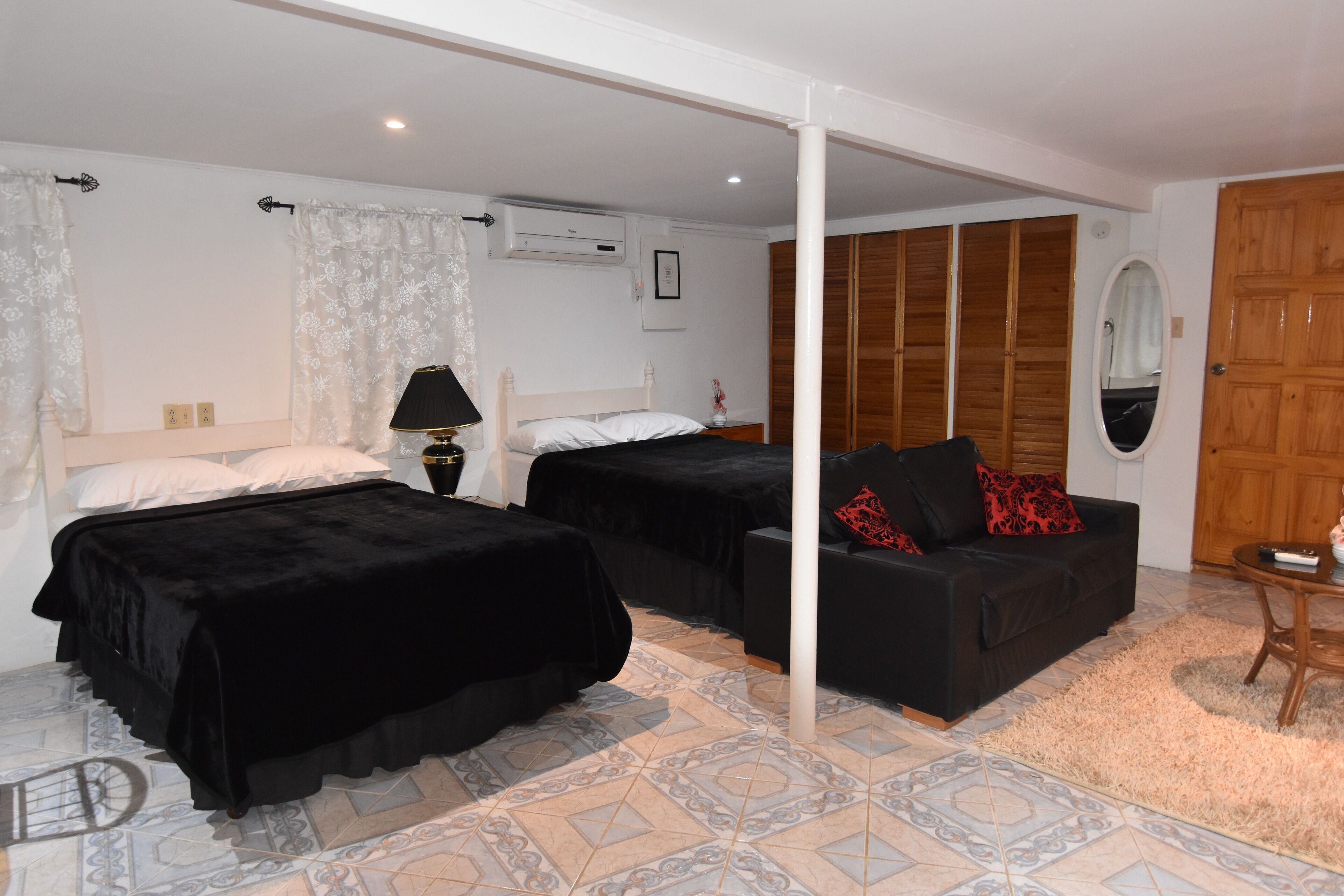 A bedroom with two beds, a sofa, a wooden wardrobe, and a mirror.