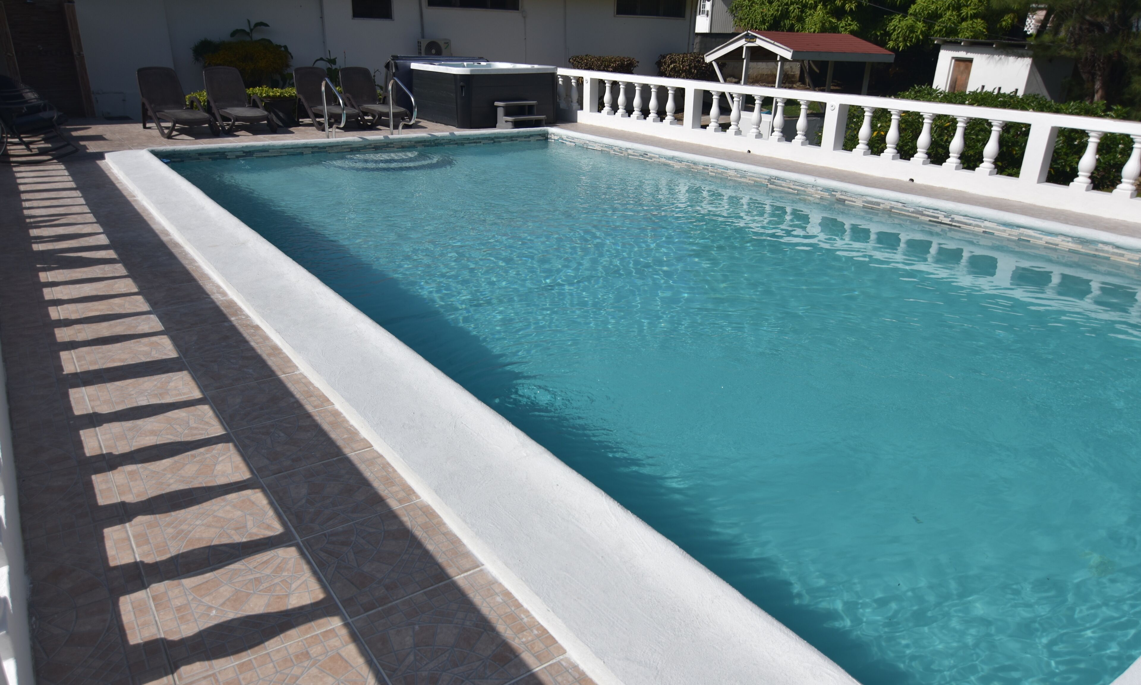 A rectangular swimming pool with a white tiled edge, surrounded by a white balustrade.