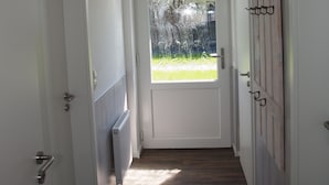 Un couloir étroit doté d’un plancher en bois, de murs blancs et d’une porte donnant sur un jardin.