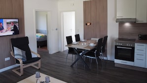 Une cuisine moderne avec un coin repas, des meubles en bois, un four encastré et un téléviseur fixé au mur.