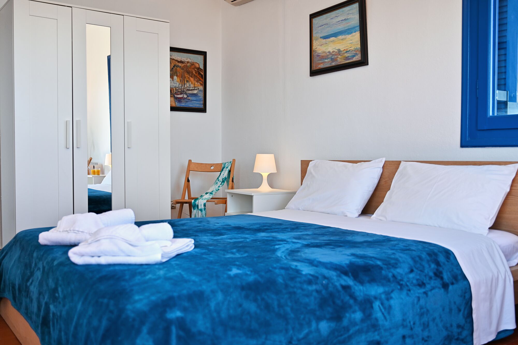 A hotel room with a bed, a chair, a nightstand, and a painting on the wall.