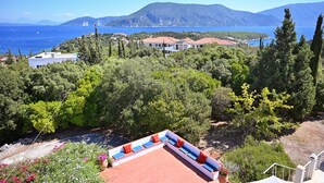 Ein Küstenanwesen mit Terrasse und Meerblick, umgeben von viel Grün und Hügeln.