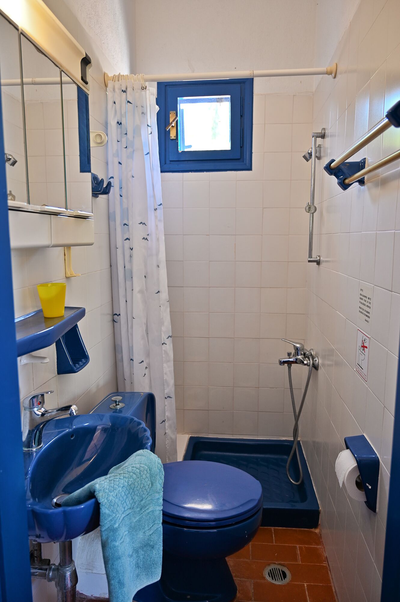 A small bathroom with a toilet, sink, and shower. There is a window above the shower, and a towel is hanging on the wall.