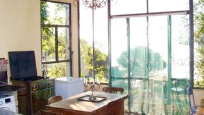 A dining area with a wooden table and chairs, a chandelier, and a view through large windows.