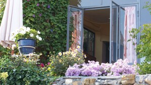 A stone wall with a potted plant and flowers in front of a building with an open door.