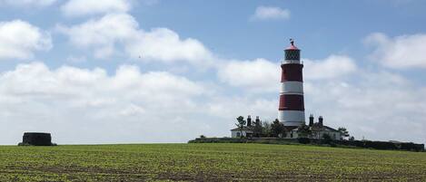 Un phare doté d’une tour rayée de rouge et de blanc, entouré d’un champ verdoyant et de quelques arbres.
