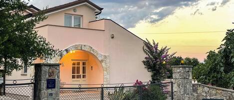 A building with a stone archway entrance, a gated driveway, and a stone wall with a plaque.