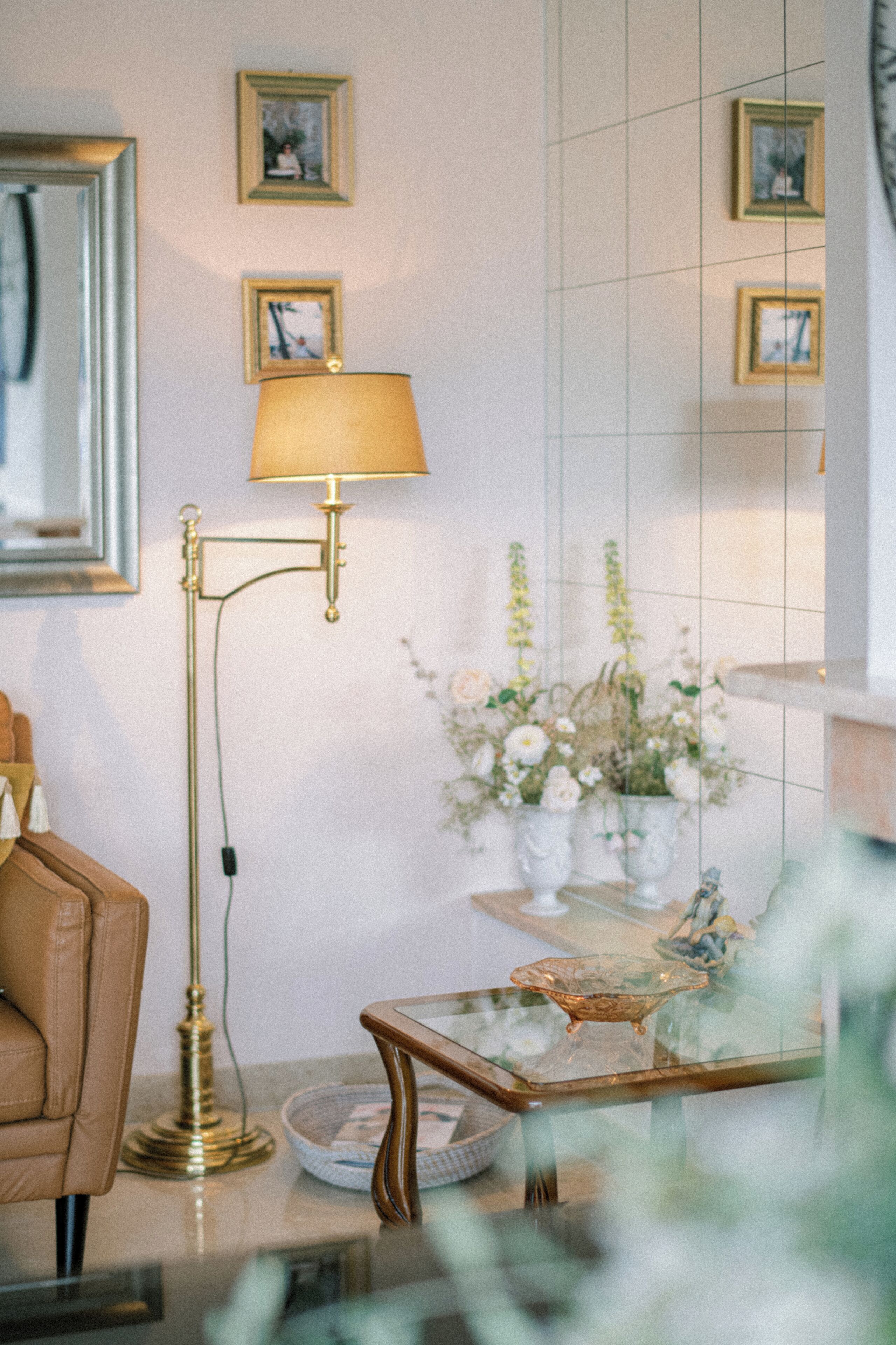 A room with a sofa, a floor lamp, a glass coffee table, and a vase with flowers.