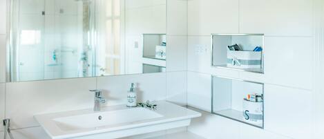 Une salle de bain moderne avec un grand miroir, un lavabo blanc et des étagères intégrées pour le rangement.