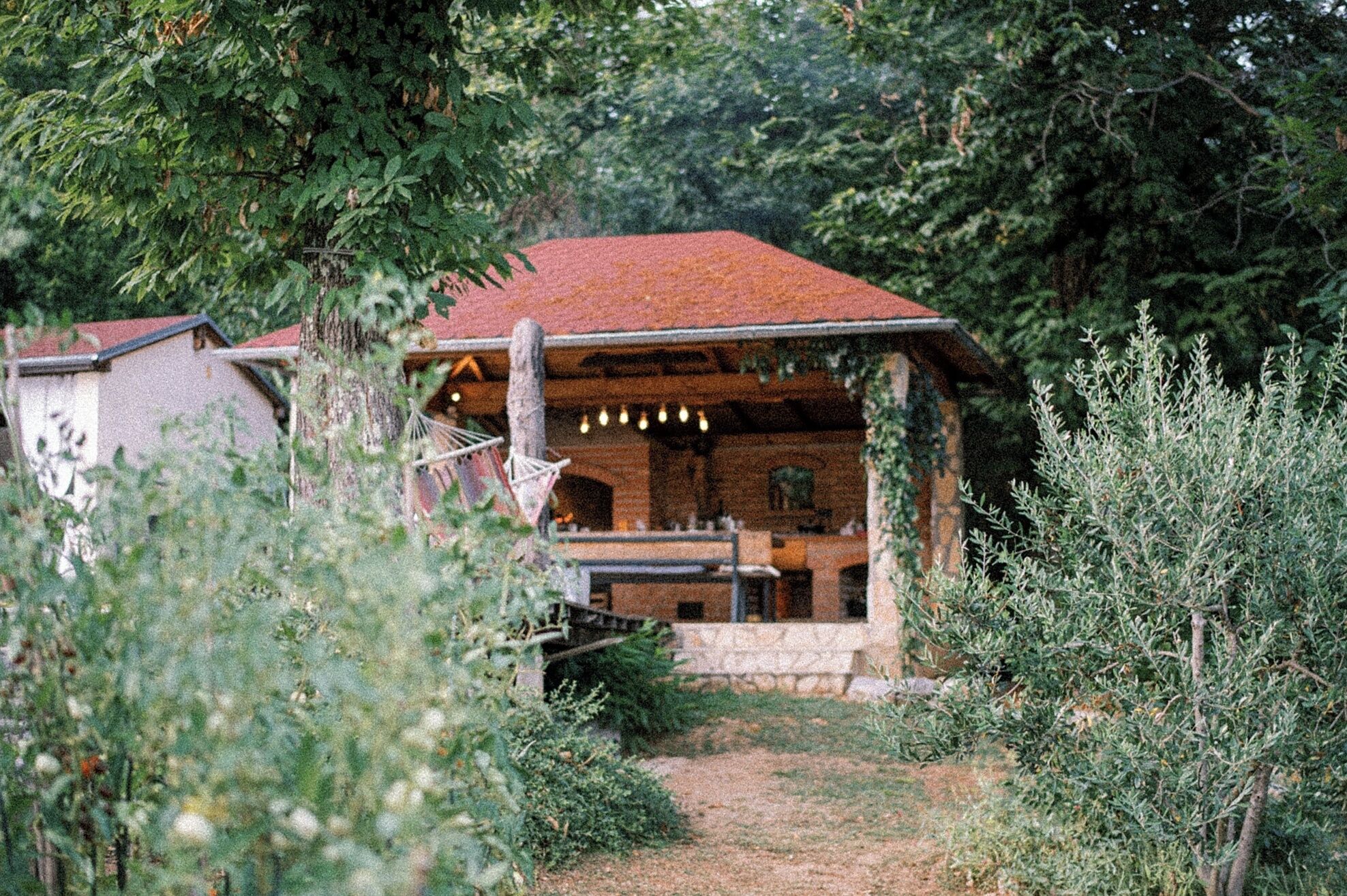 A rustic cabin with a red roof, surrounded by dense greenery.