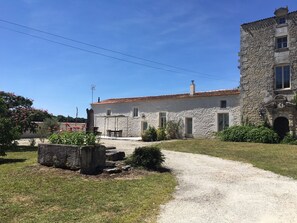 A stone building with a tiled roof, a gravel path, and a garden with flowers and shrubs.