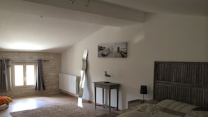 A bedroom with a large bed, a radiator, a window with curtains, a wall-mounted artwork, and a small table with a bird sculpture. - Unique! A seigneury of the 17th century, completely renovated, 20 minutes from the beach (Thaims)