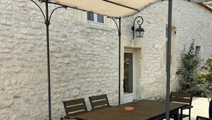 An outdoor patio with a table and chairs, a stone wall, and a covered area with a metal frame. - Unique! A seigneury of the 17th century, completely renovated, 20 minutes from the beach (Thaims)