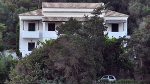 Um edifício de dois andares com telhado em telhas, rodeado por uma floresta densa.