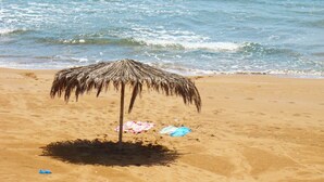 Uma praia com um guarda-sol de palha, uma toalha e algas na areia.