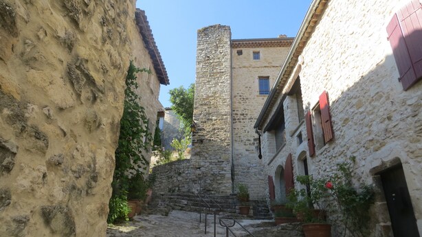 A narrow cobblestone street flanked by historic stone buildings with arched windows and a central stone tower. - Le Mas des Restanques 3*,located in one of the most beautiful villages in France (Le Poët-Laval)