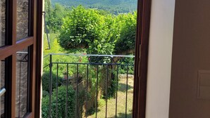 A balcony with a stone wall, a metal railing, and a view of green hills and a clear blue sky. - Le Mas des Restanques 3*,located in one of the most beautiful villages in France (Le Poët-Laval)