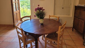 A dining area with a round wooden table, four wooden chairs, a vase with flowers, a decorative mirror, and a view of greenery through a window. - Le Mas des Restanques 3*,located in one of the most beautiful villages in France (Le Poët-Laval)