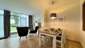 A dining area with a wooden table and chairs, a hanging light fixture, and framed pictures on the wall.