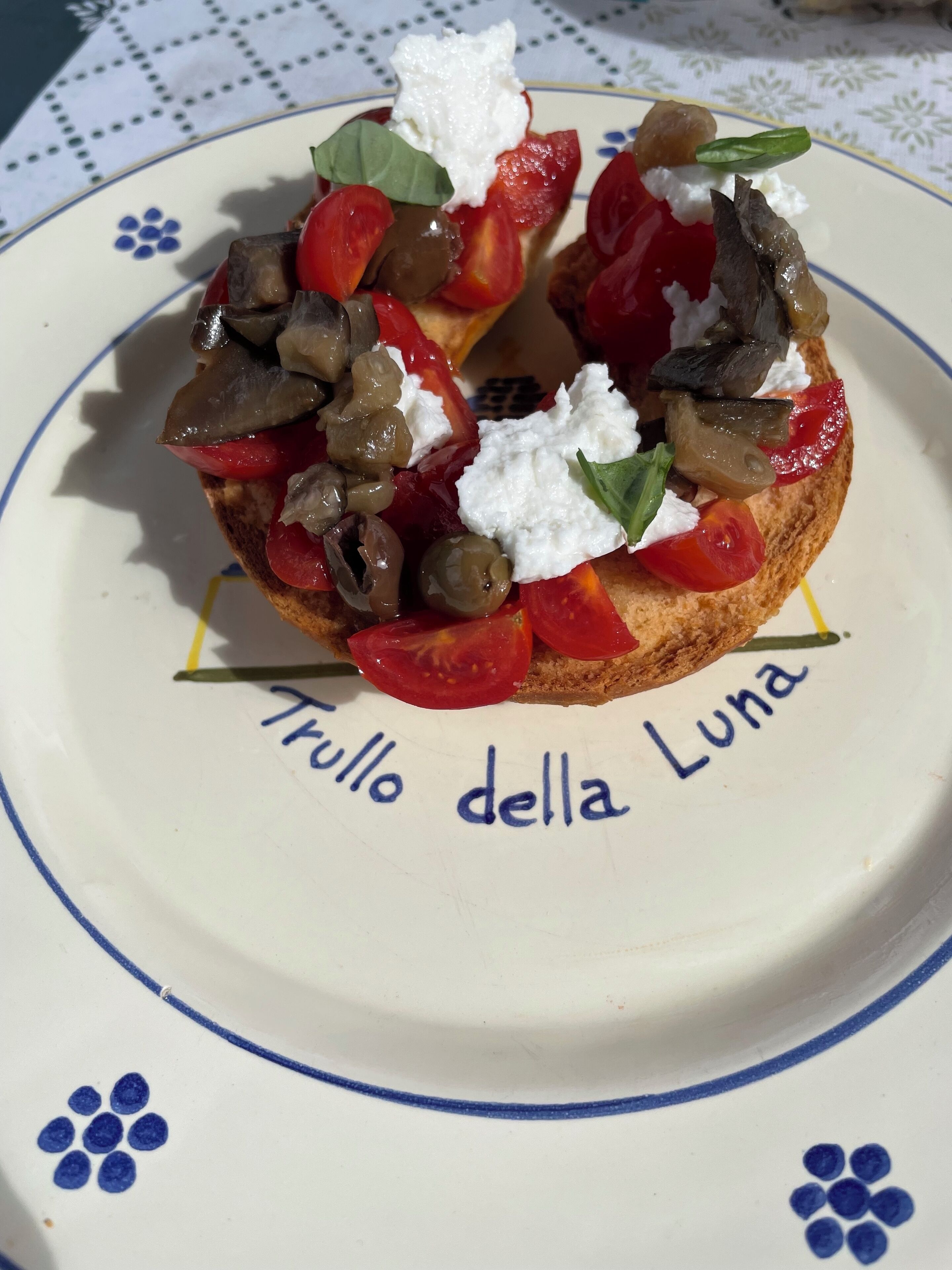 A plate with a sandwich topped with tomatoes, olives, and feta cheese, labeled "Trullo della Luna".