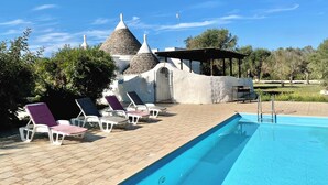 Un espace aménagé au bord de la piscine, avec des chaises longues, une piscine et un bâtiment doté de toits coniques.