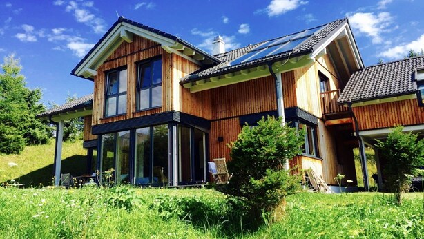 A two-story wooden house with large windows and a balcony.
